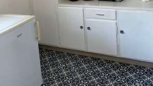 Une cuisine de taille réduite, avec des meubles blancs, un petit réfrigérateur et un carrelage décoratif.