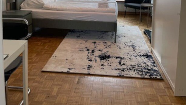 Une chambre moderne avec un lit, un bureau, une chaise, une grande fenêtre et un luminaire suspendu.