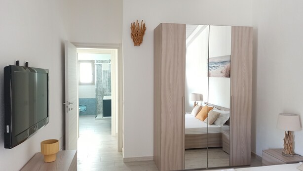 A modern bedroom with a large wardrobe, a television, and a bedside table with a lamp. - Villa 21 - A - Two Bedroom Villa, Sleeps 4 (Budoni)