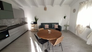 A modern kitchen with a built-in oven, a dining table with chairs, and a sofa in the living area. - Villa 21 - A - Two Bedroom Villa, Sleeps 4 (Budoni)