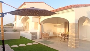 A patio with a table and chairs, an umbrella, and a small garden area with stepping stones. - Villa 21 - A - Two Bedroom Villa, Sleeps 4 (Budoni)