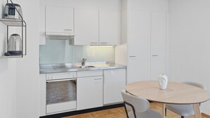 A modern kitchen with white cabinets, a stainless steel sink, and a round table with two chairs. - Charming studio in the city centre (Art 21) (Zürich)