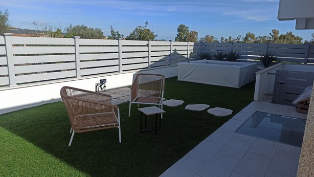 A patio with artificial grass, a wicker chair, a small table, a white fence, and a pool area. - Villa 21 - B - Two Bedroom Villa, Sleeps 4 (Budoni)