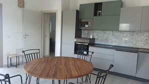 A compact kitchen with a round wooden table and four chairs, a microwave, and a built-in oven. - Villa 21 - B - Two Bedroom Villa, Sleeps 4 (Budoni)