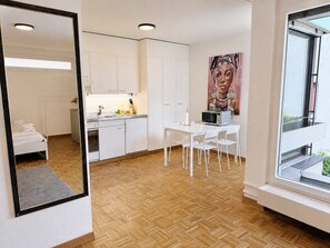 A modern kitchen with white cabinets, a dining area with a white table and chairs, and a large window with a view. - Practical studio in the city center (Art 7) (Zürich)