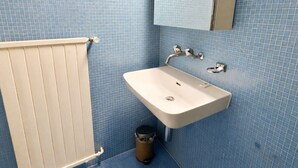 A bathroom with a white sink, a mirror, and a radiator. - Practical studio in the city center (Art 7) (Zürich)