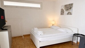 A bedroom with a bed, a desk, a lamp, and a wall-mounted artwork. - Practical studio in the city center (Art 7) (Zürich)