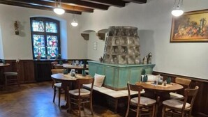 A restaurant with wooden herringbone flooring, wooden tables and chairs, a stained glass window, and a decorative wall feature. - Hotel Roß (Zwoenitz)