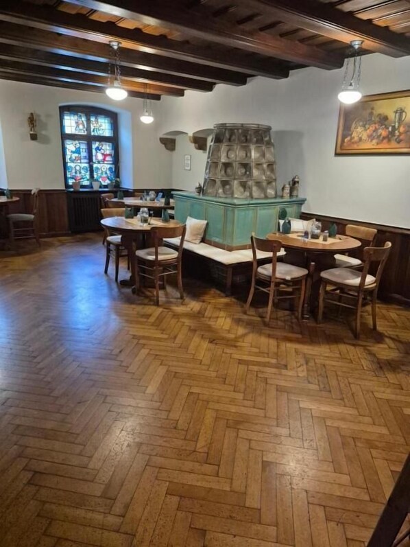 Un restaurante con suelo de madera en espiga, mesas y sillas de madera, un ventanal de vitrales y un elemento decorativo en la pared.