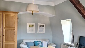 A cozy loft-style room with a wooden ceiling, a white sofa, a wooden cabinet, and a small table. - Hotel Roß (Zwoenitz)
