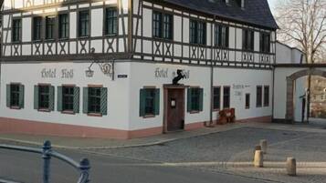 A traditional half-timbered building with "Hotel Hof" signage, a cobblestone street, and a metal railing in the foreground.