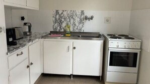 Une cuisine compacte avec des meubles blancs, un pare-feu en marbre, une cuisinière encastrée et un évier.