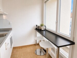 A compact kitchen with a black countertop, white stools, and a window providing natural light.