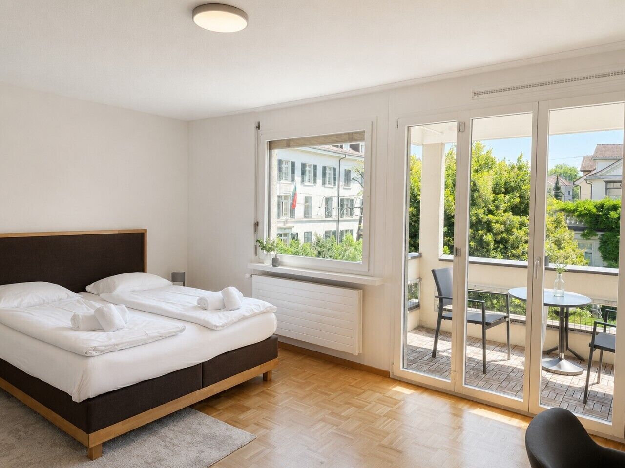 A hotel room with a bed, a window, and a balcony with chairs and a table.