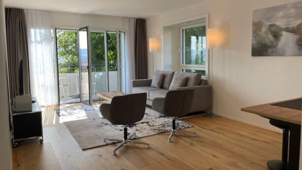 Una sala de estar moderna con un sofá, una mesa de centro y una mesa de comedor. Hay un ventanal corredero que da a un balcón.