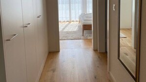 Un estrecho pasillo con piso de madera que conduce a un dormitorio con cama y un amplio ventanal.