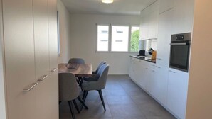 Una cocina moderna con armarios blancos, una mesa de comedor con sillas y un horno empotrado.