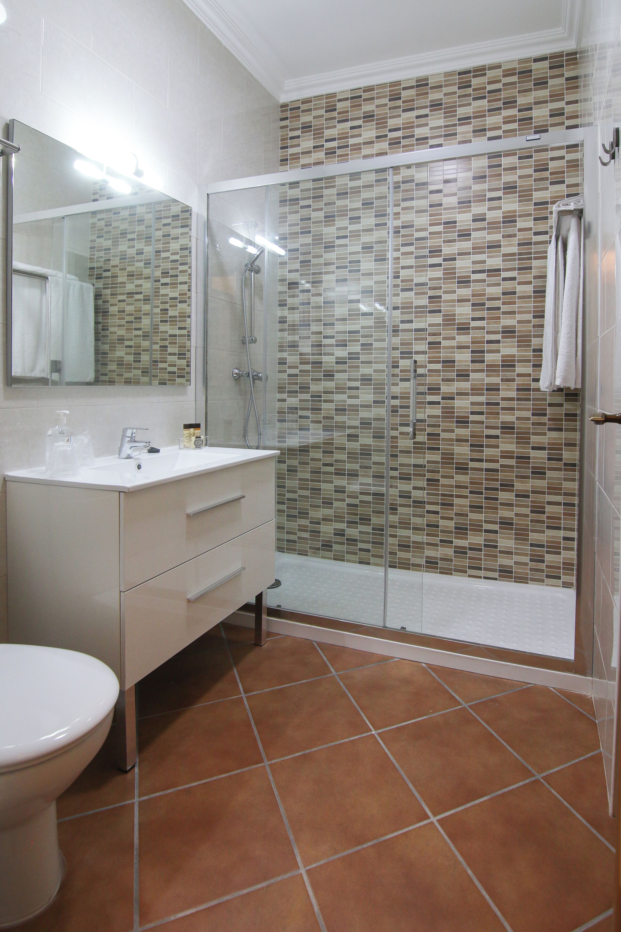 Un bagno con un mobile lavabo bianco, cabina doccia in vetro e pavimento piastrellato.