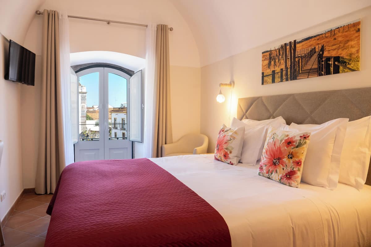Ein Hotelzimmer mit einem großen Bett, Blick durch eine Tür, einem Bild an der Wand und einem Sessel.