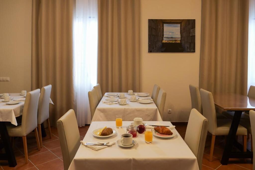 Uma sala de jantar com mesas preparadas para o café da manhã, incluindo pratos, copos e suco.
