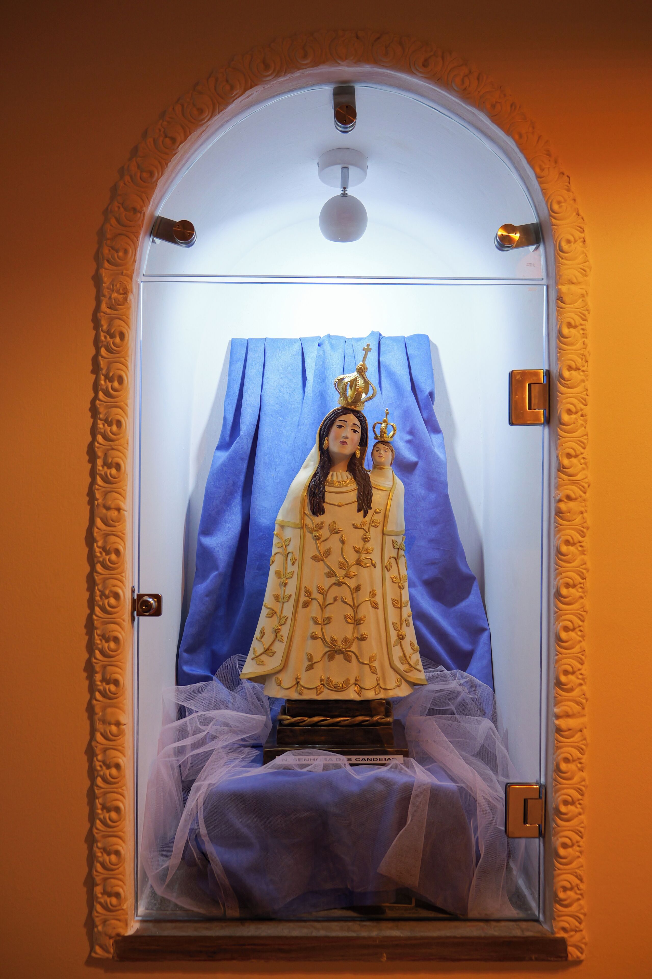 Uma estátua religiosa em uma moldura com um fundo de cortina azul.