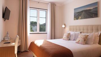 A hotel room with a bed, a desk with a chair, a TV, and a painting on the wall.