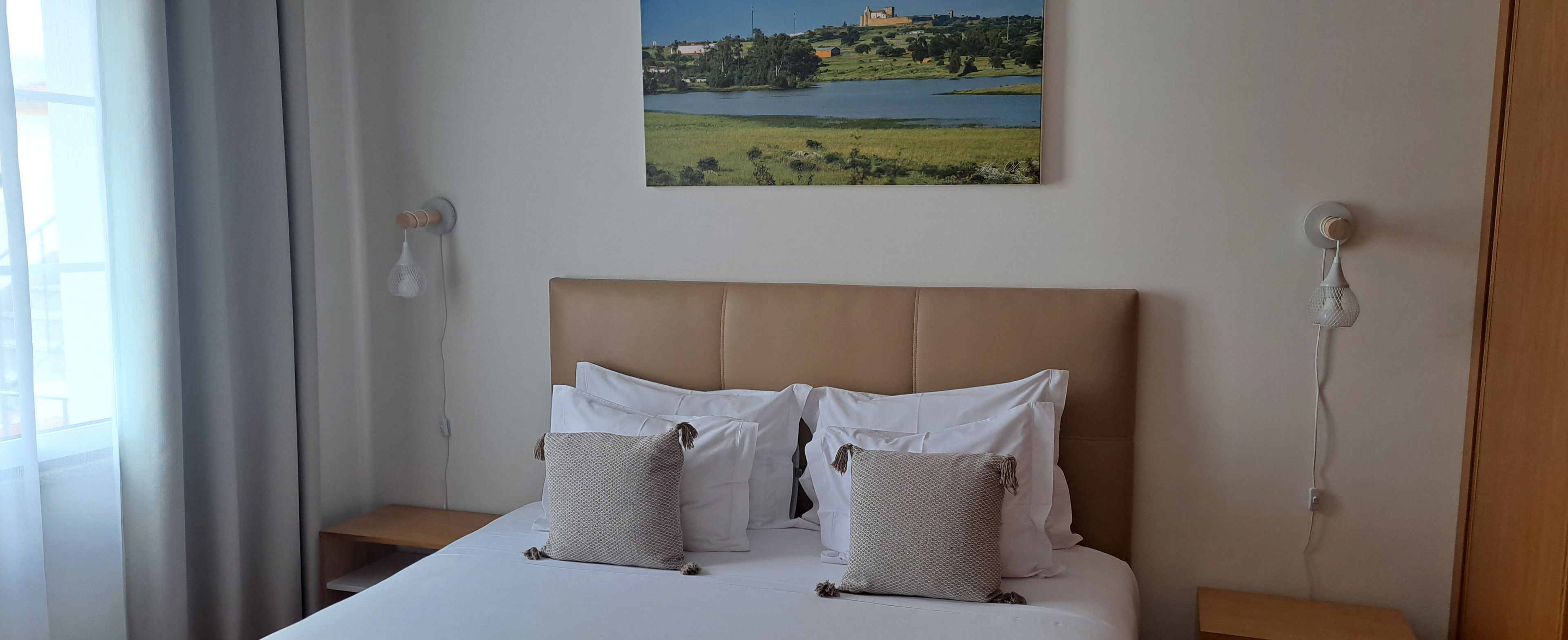 Ein Hotelzimmer mit einem Bett, zwei Nachttischen, einem Landschaftsbild und einem Fenster mit Vorhängen.
