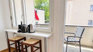 A room with a white desk, two wooden chairs, a window, and a view of a building outside.