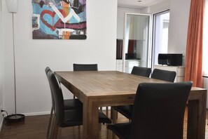 A dining area with a wooden table and black chairs, a painting on the wall, and a kitchen visible through an open door. - Stylish 1BR near lake and Opera (Flower 52) (Zürich)