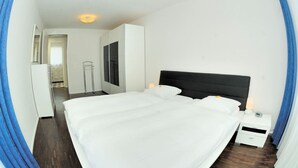 Quarto de hotel moderno com uma cama grande, uma mesinha de cabeceira, um guarda-roupa e um espelho.
