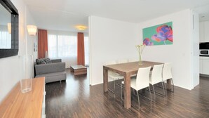 Uma sala de estar moderna com um sofá, uma mesa de jantar com cadeiras, uma mesa de centro e um quadro na parede.