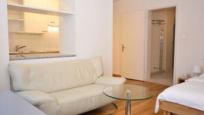 A modern hotel room with a glass table, a white sofa, a bed, a shower, and a kitchen area visible through an open door. - Nice studio in the city center (Vineyard 11) (Zürich)