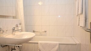 A bathroom with a white sink, a bathtub, and a mirror. - Nice studio in the city center (Vineyard 11) (Zürich)