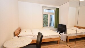 A small, clean room with two single beds, a TV, a small table, and a chair.