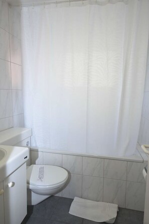 Een kleine, schone badkamer met toilet, wastafel en douchegordijn.