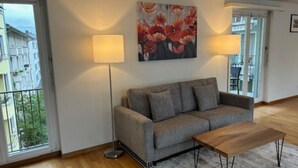 A living room with a grey sofa, two floor lamps, a wooden coffee table, and a large floral painting on the wall. - Cozy 1 bedroom in the center (D11) (Zürich)