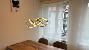 A dining area with a wooden table and four chairs, a pendant light, and a window with a view of buildings. - Cozy 1 bedroom in the center (D11) (Zürich)