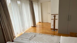 A hotel room with a large bed, wooden flooring, a wardrobe, and a door leading to another room. - Cozy 1 bedroom in the center (D11) (Zürich)