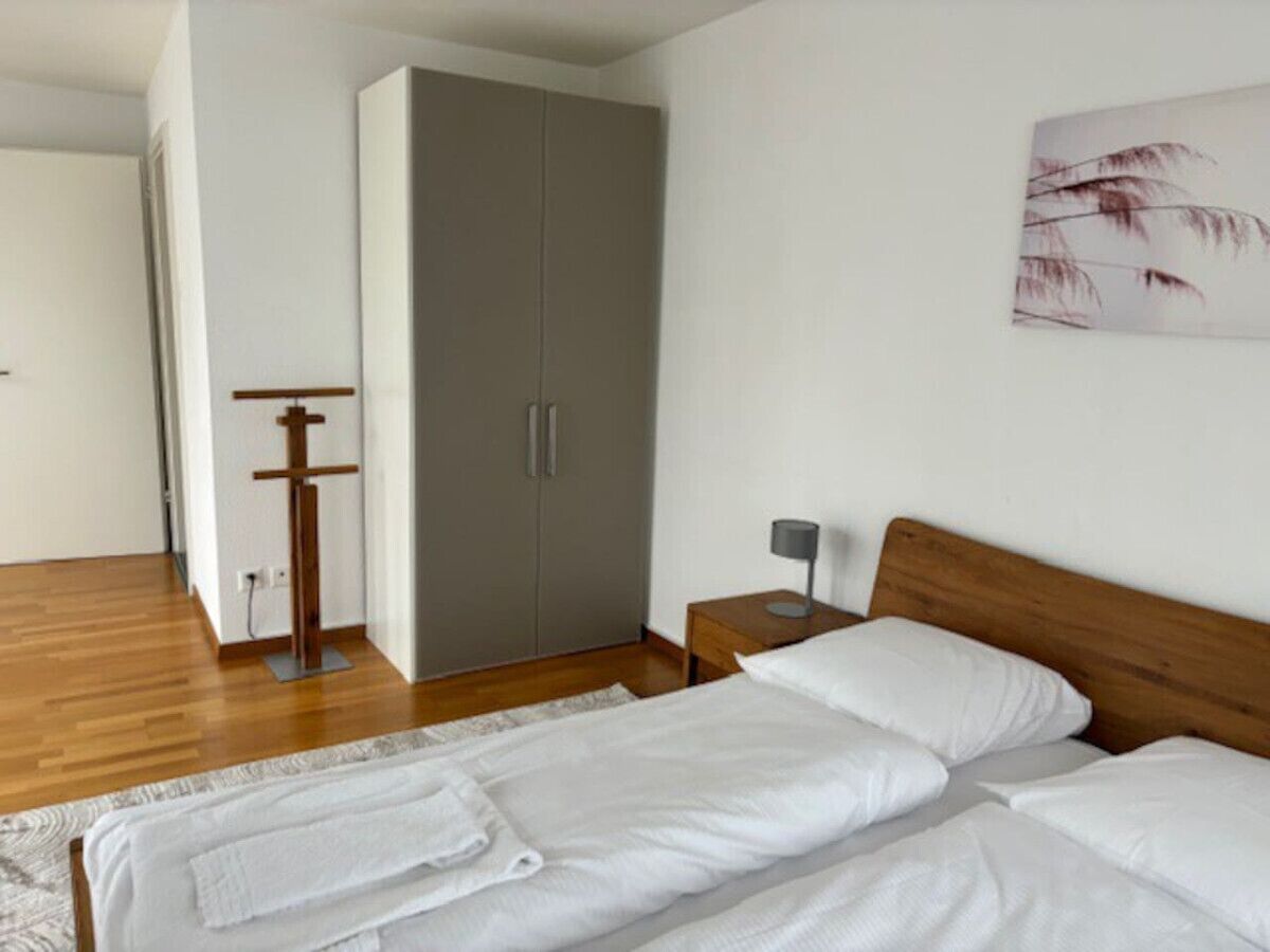 Ein Schlafzimmer mit einem hölzernen Bett, einem grauen Schrank, einem Nachttisch mit Lampe und einem an der Wand hängenden Kunstwerk.
