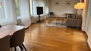 A spacious living area with a wooden floor, a dining table with chairs, a sofa, a TV, and a lamp. - Cozy 1 bedroom in the center (D11) (Zürich)