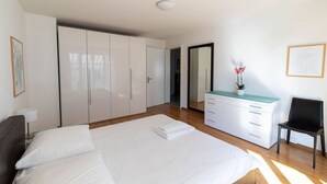 A bedroom with a large bed, a wardrobe, a desk with drawers, a chair, and a mirror.
