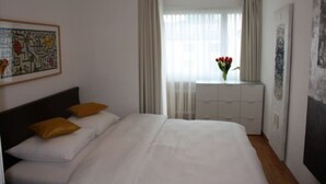 Habitación de hotel con cama, mesita de noche, ventana con cortinas y un cuadro en la pared.