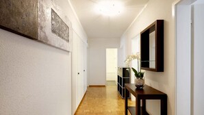 A hallway with a wooden floor, white walls, and a dark wooden console table with a vase of flowers.