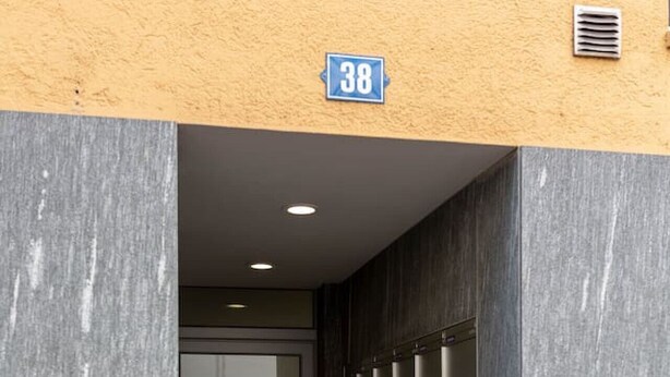 A building entrance with a blue sign displaying the number 38, a door, and a wall with a grid of small windows.