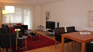 A modern living room with a sofa, coffee table, TV, and dining area.