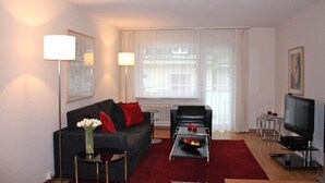 A modern living room with a dark sofa, a red-rugged coffee table, a TV, and a radiator.