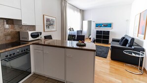 Een moderne keuken met witte kastjes, een magnetron en een oven. Er is een zithoek met een zwarte bank en een kleine tafel.