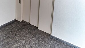 Een smalle gang met een beige lift en een deur met een klein bordje.