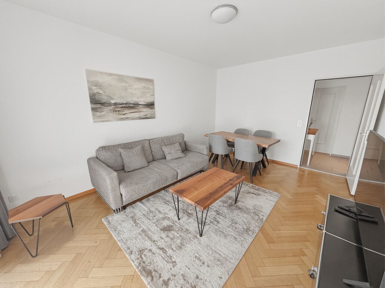 A modern living room with a sofa, coffee table, rug, and dining area.