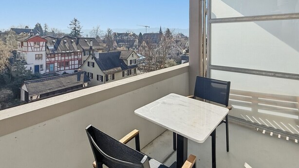 Un balcón con mesa y sillas, con vistas a una zona residencial con casas tradicionales.